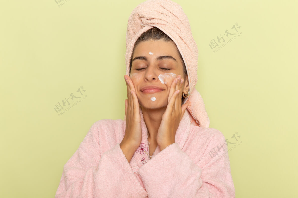 前面正面图穿着粉色浴袍的年轻女性在浅绿色表面涂面霜浴衣衣服浴巾