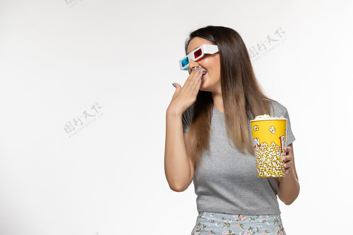 电影院正面图年轻女性手持爆米花 戴着d型太阳镜在浅白色的表面上看电影抱着孤独漂亮