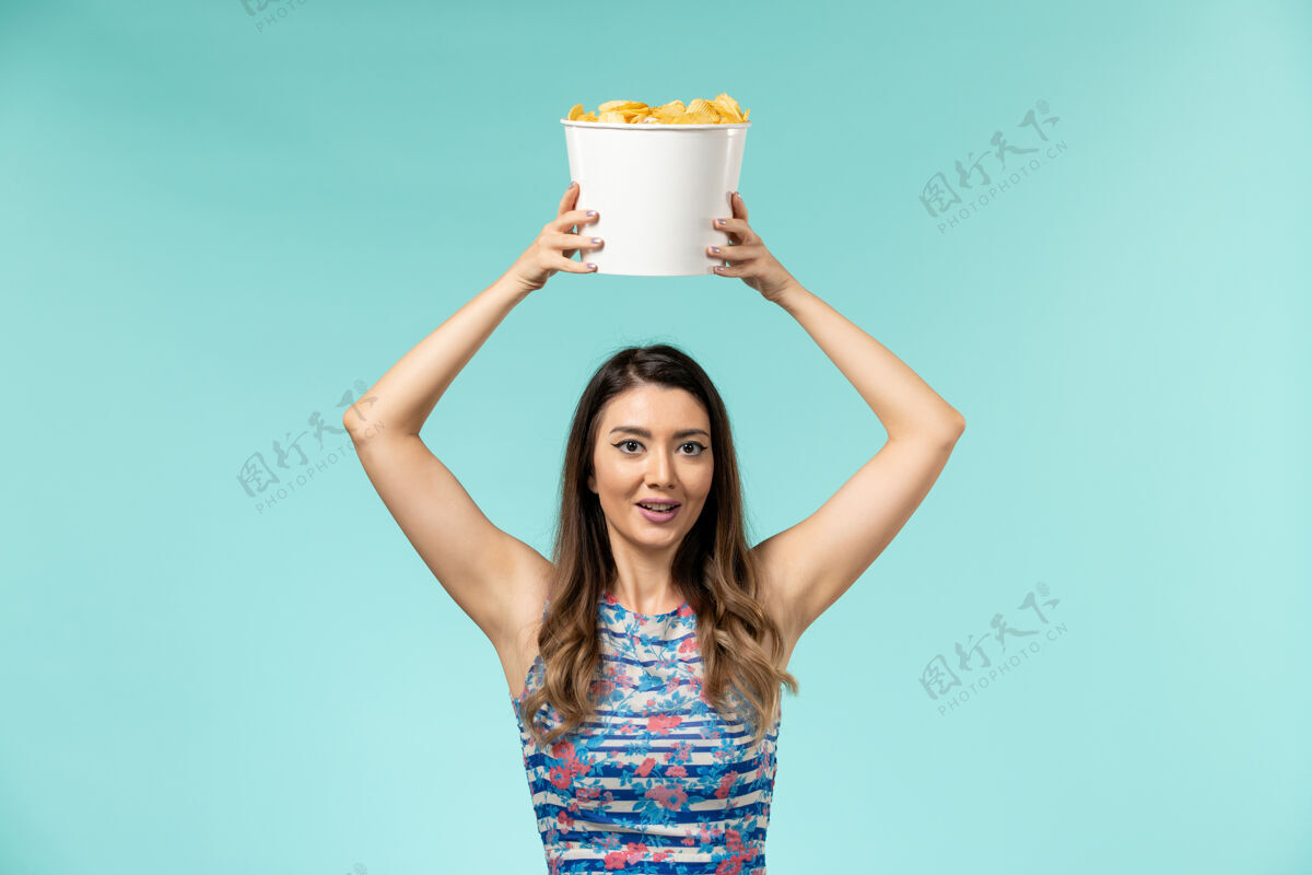 抱正面图：年轻的女性拿着篮子和薯片 在蓝色的水面上看电影前面篮子电影