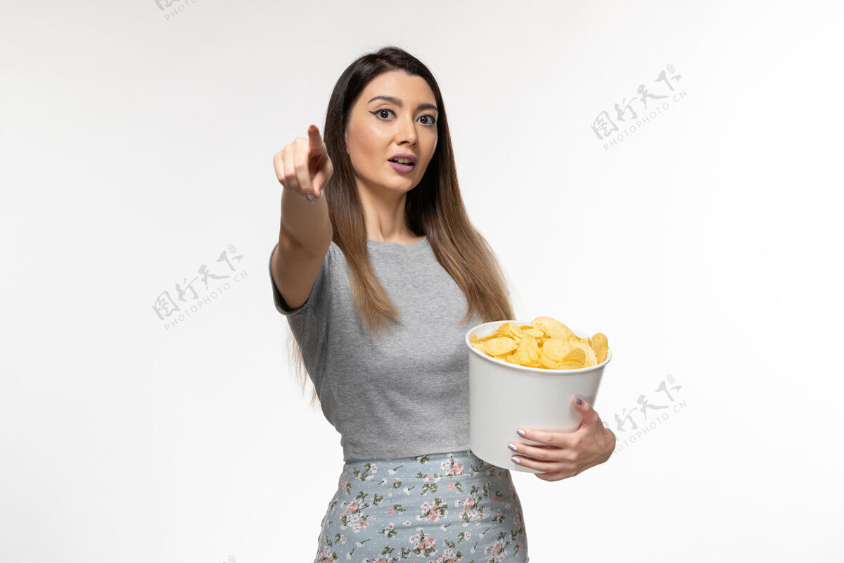 年轻女性正面图：年轻女性在白色表面上吃薯片看电影看黑发土豆