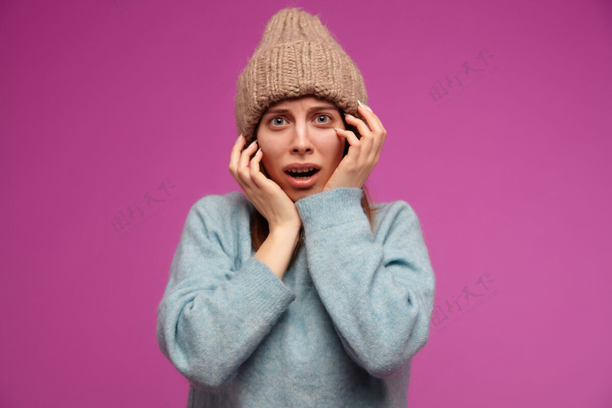 心情十几岁的女孩 一头深褐色长发 面色恐惧 穿着蓝色毛衣 戴着针织帽子 在紫色的墙上恐惧地抚摸着她的脸女士毛衣女孩