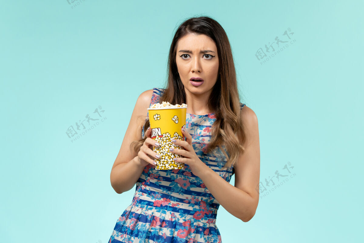 举行正面图：年轻女性手持爆米花包 在蓝色表面看电影爆米花包装看