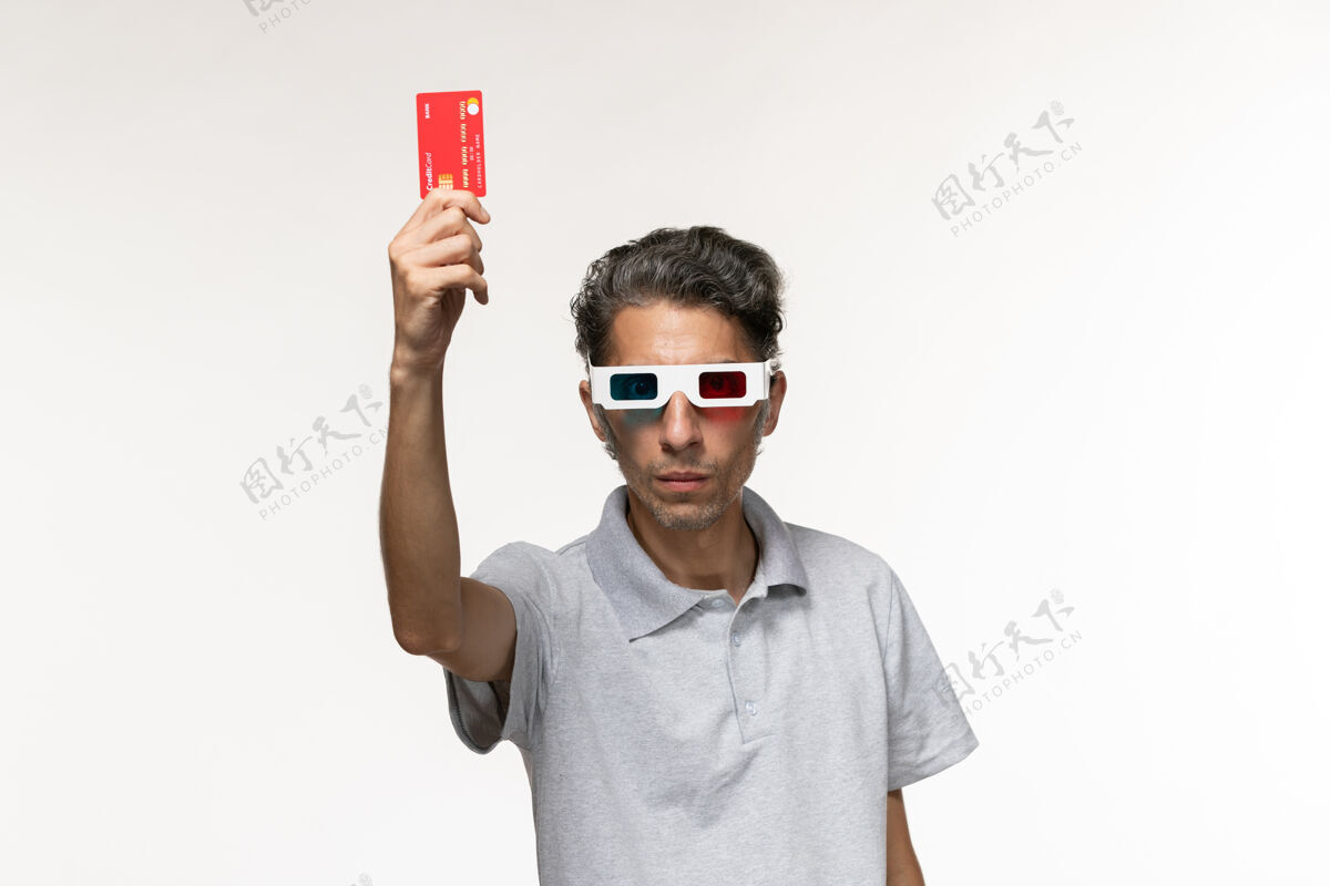 银行正面图年轻男子手持红色银行卡 戴着d型太阳镜 表面呈浅白色太阳镜享受浅白色