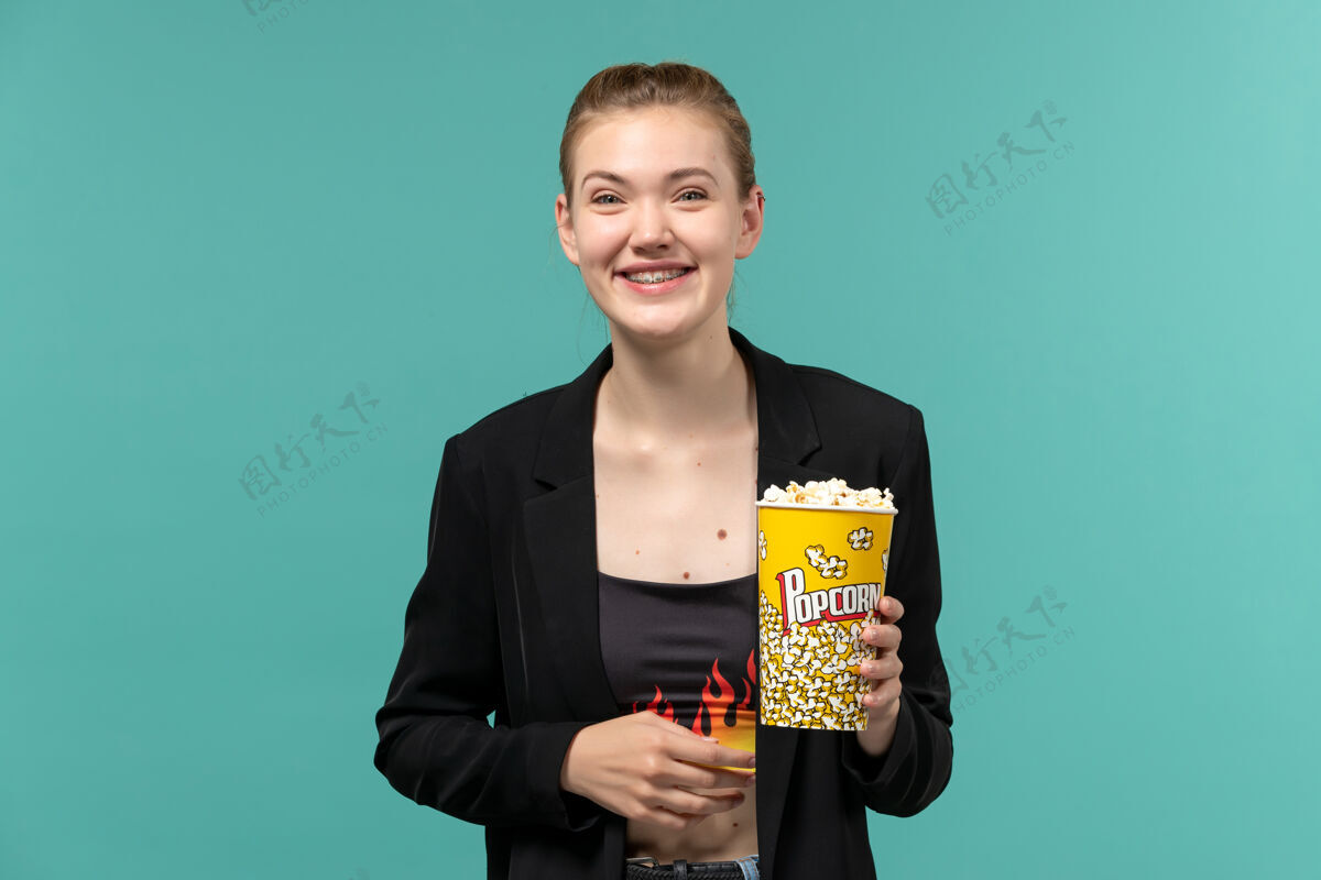 电影正面图：年轻女子拿着爆米花包 在蓝色的水面上看电影大笑电影电影院年轻的女性