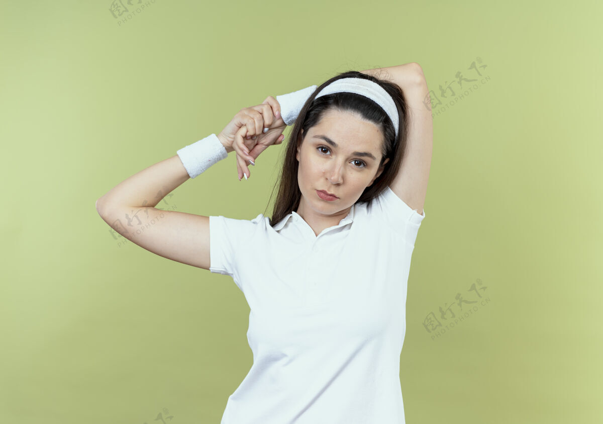手戴着头巾的年轻健身女士站在轻薄的墙上 双手叉开 看起来很自信轻年轻站立