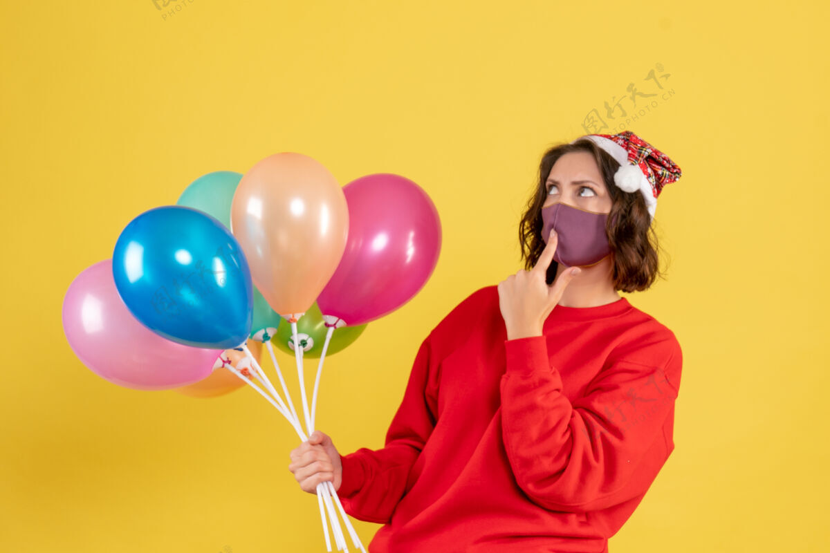 正面正面图：戴着黄色面具手持气球的年轻女子外科面具女人气球