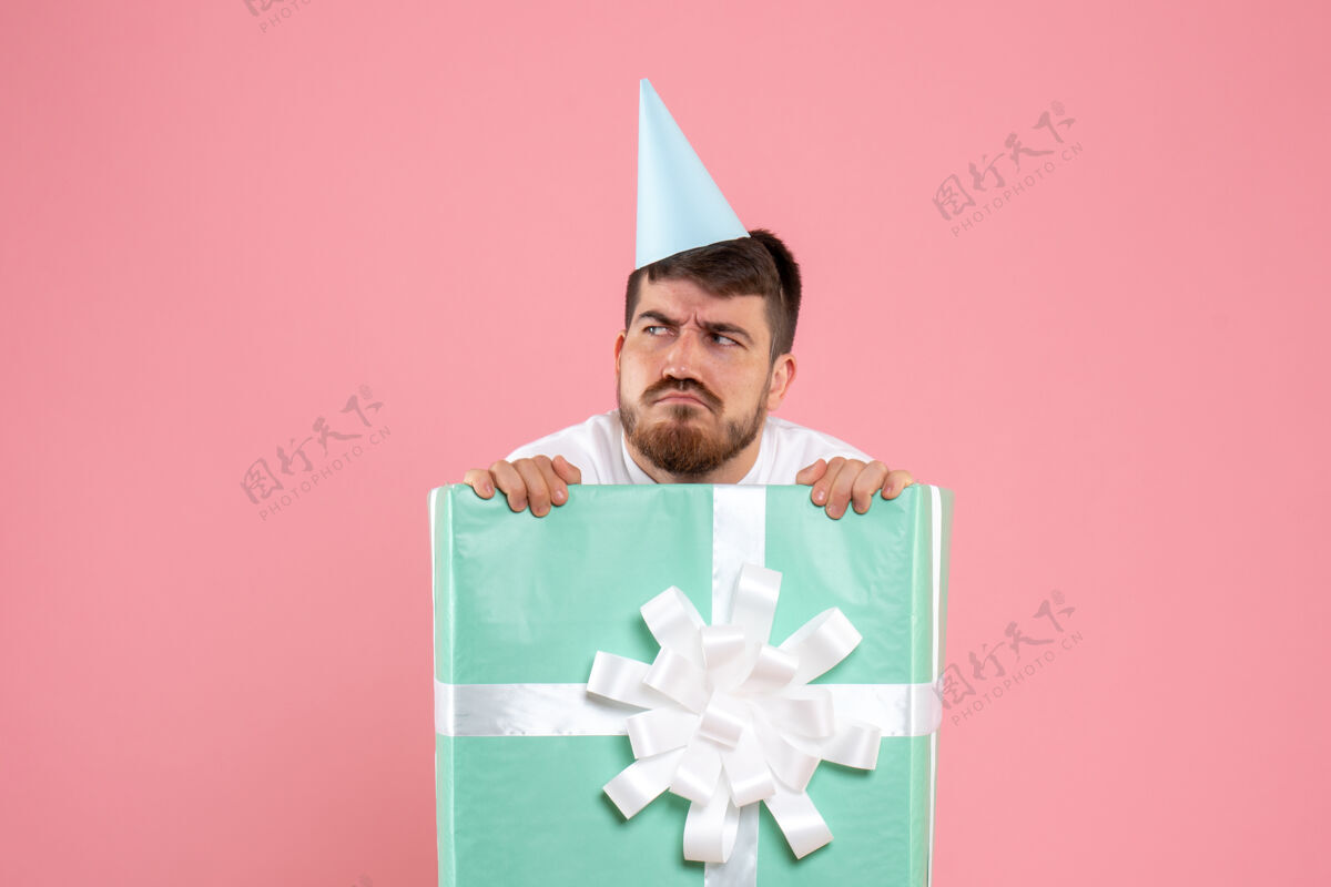 立场正面图：年轻男性站在礼品盒内的粉红色圣诞照片情感人类头饰人类礼物