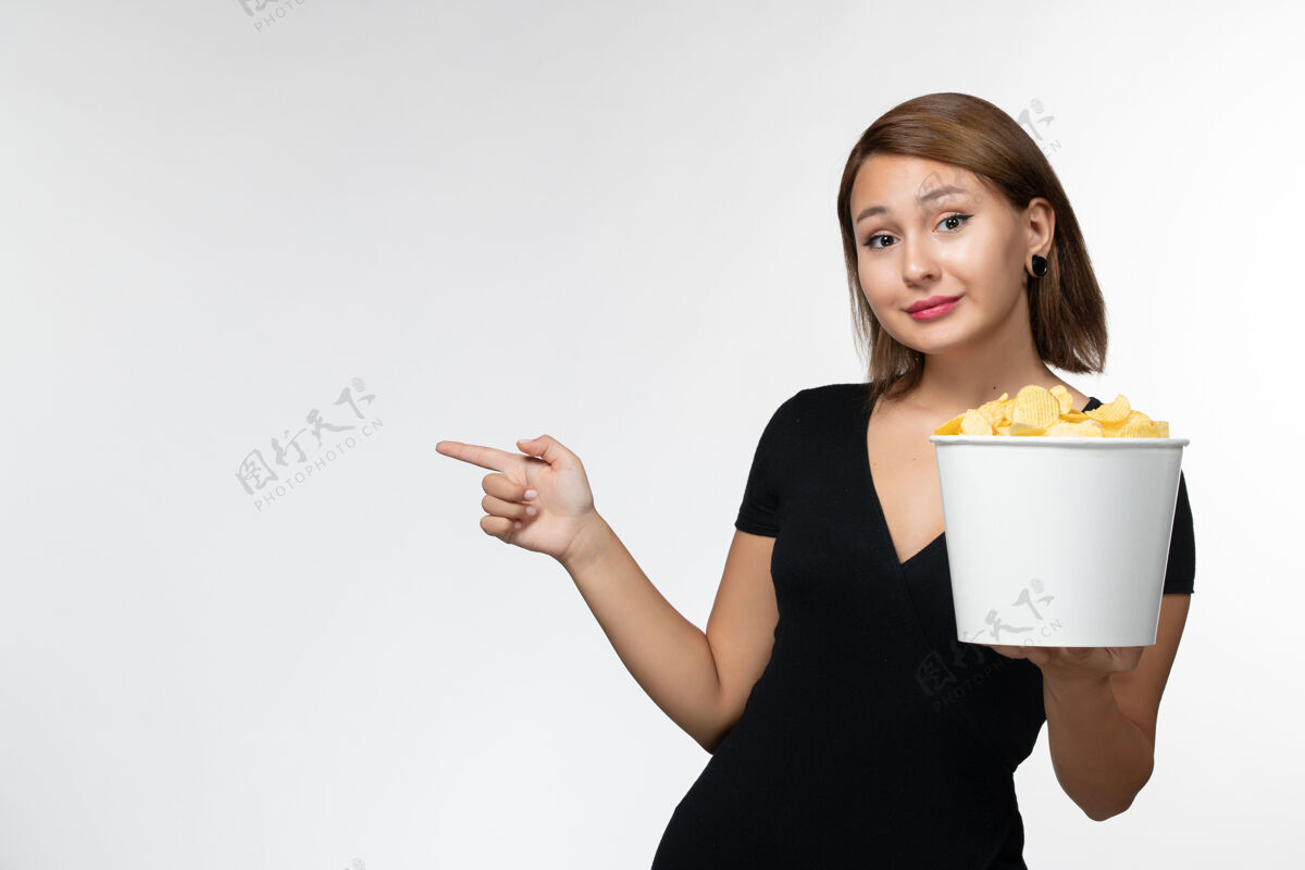 前面正面图身穿黑色衬衫的年轻女性在白色表面上拿着薯片孤独年轻的女性电影