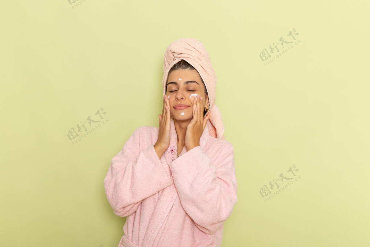 书桌正面图穿着粉红色浴袍的年轻女性在绿色的桌子上涂面霜年轻女性自我护理浴袍