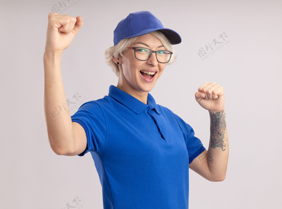 自信身着蓝色制服 高举双拳的年轻女送货员站在白色的墙上 快乐而自信举起站立女人