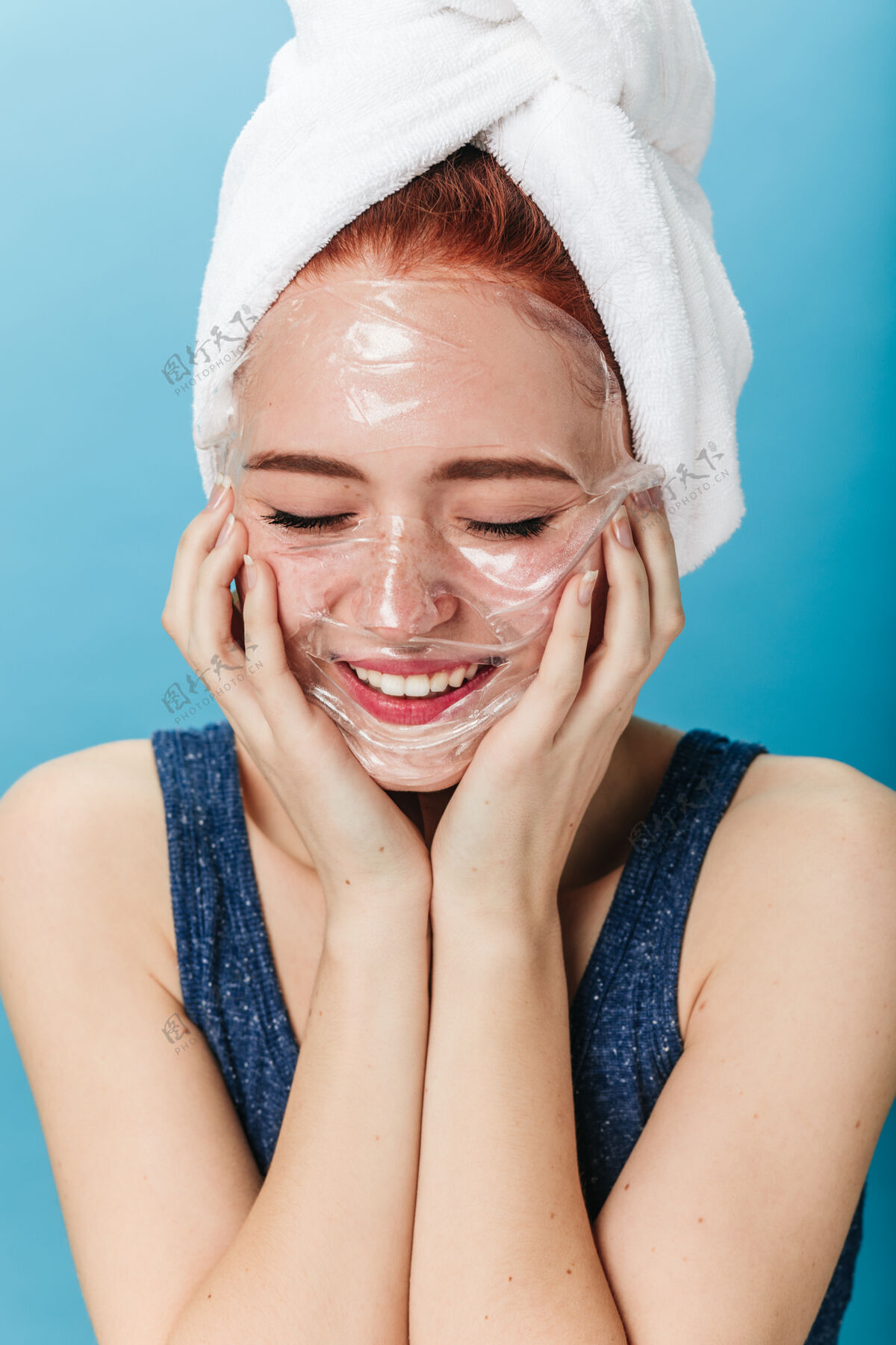 自然积极的白人女孩做水疗与微笑工作室拍摄的快乐的女人应用面膜隔离在蓝色背景上皮肤护理水疗美容