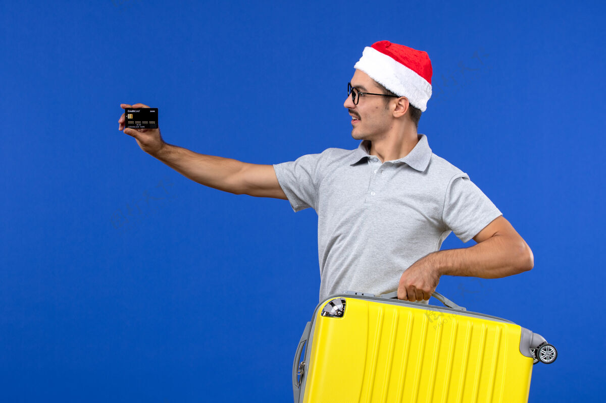 圣诞节前视图年轻男性携带包和银行卡在蓝墙航班度假飞机球员视图包