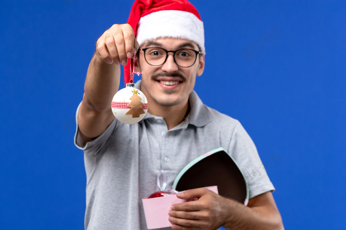 视图正面图：年轻男性手持塑料树玩具在蓝色背景上过年圣诞节球员微笑