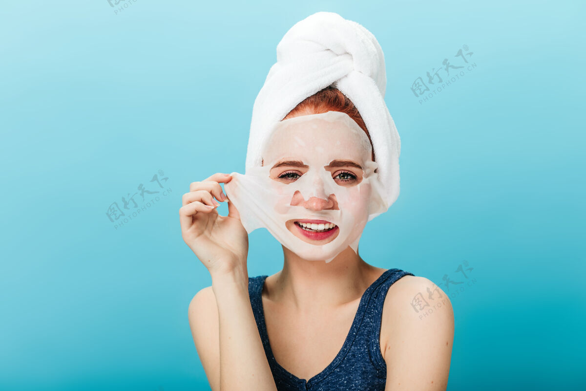 擦洗微笑的女孩摘下面罩的正面图蓝色背景下 头上戴着毛巾的幸福女人的摄影棚照片面部女孩美容