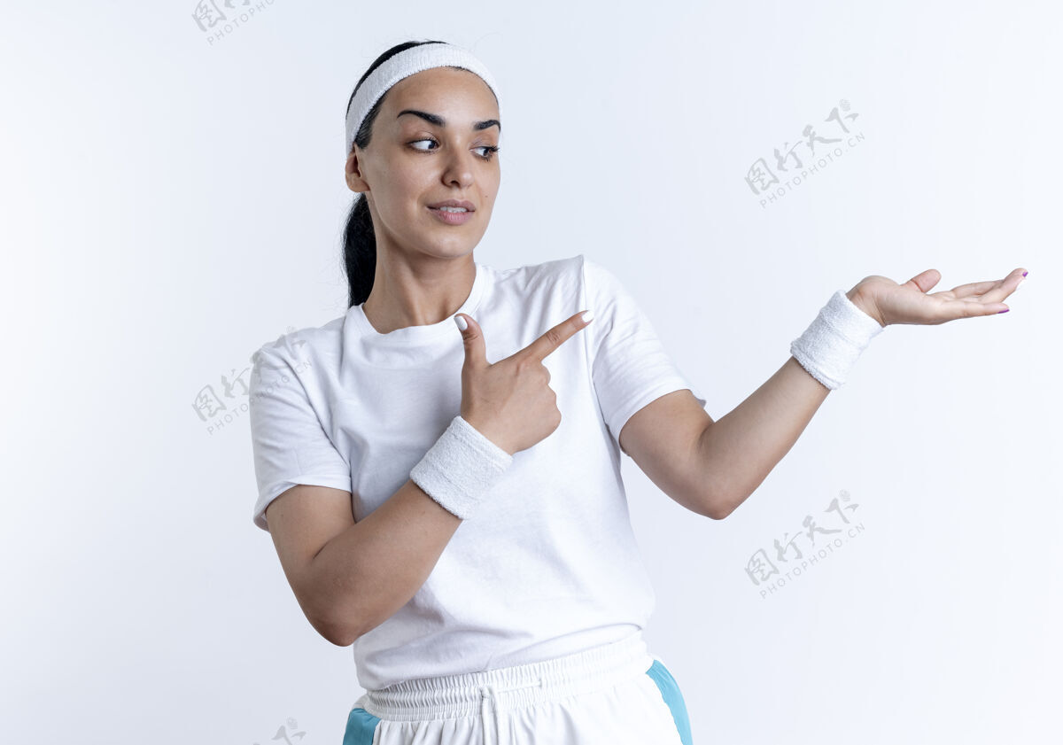 穿年轻自信的高加索运动女性戴着头带和腕带指着空空的手 隔离在空白的空间和复制空间手空间女人
