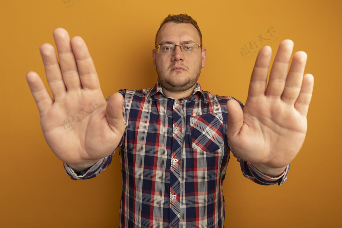 开戴着眼镜和格子衬衫的男人站在橙色的墙上 张开双手 严肃地做着停止的手势男人认真手势