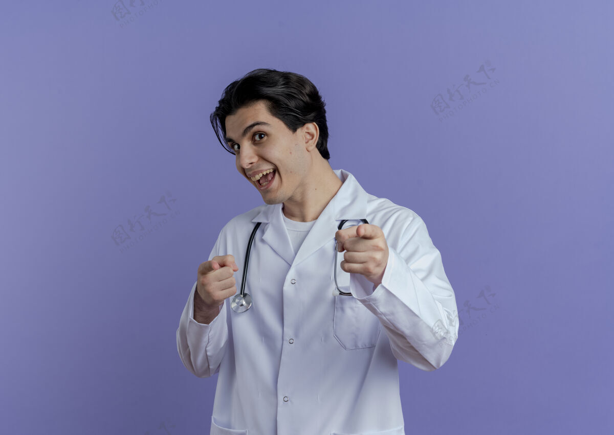 医疗印象深刻的年轻男医生穿着医用长袍和听诊器做你的手势隔离在紫色的墙上与复制空间表情穿着听诊器
