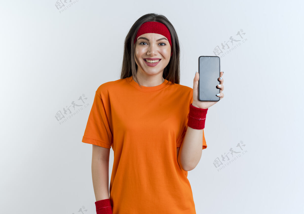 微笑微笑的年轻运动女性戴着头带和腕带展示手机电话运动腕带
