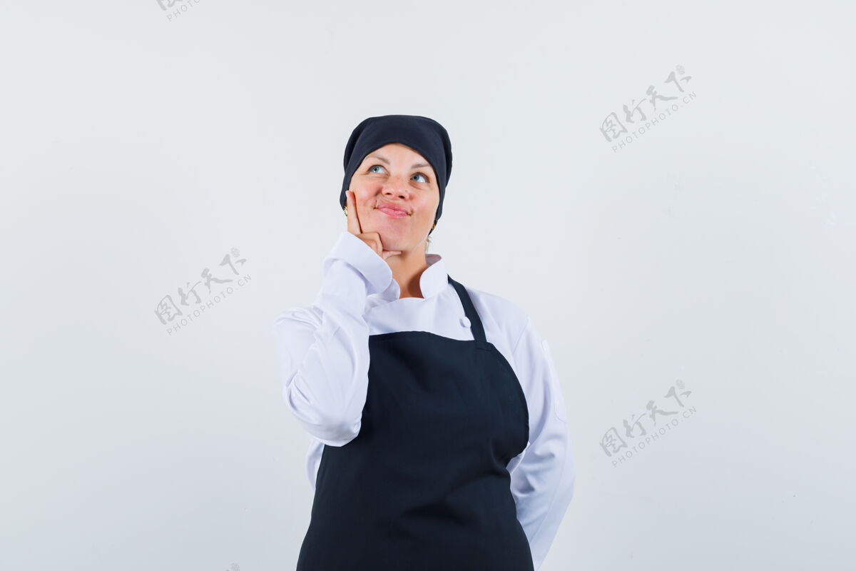 女性金发女人把食指放在脸颊上 想着穿黑色厨师制服的东西 看起来很漂亮黑发放护理