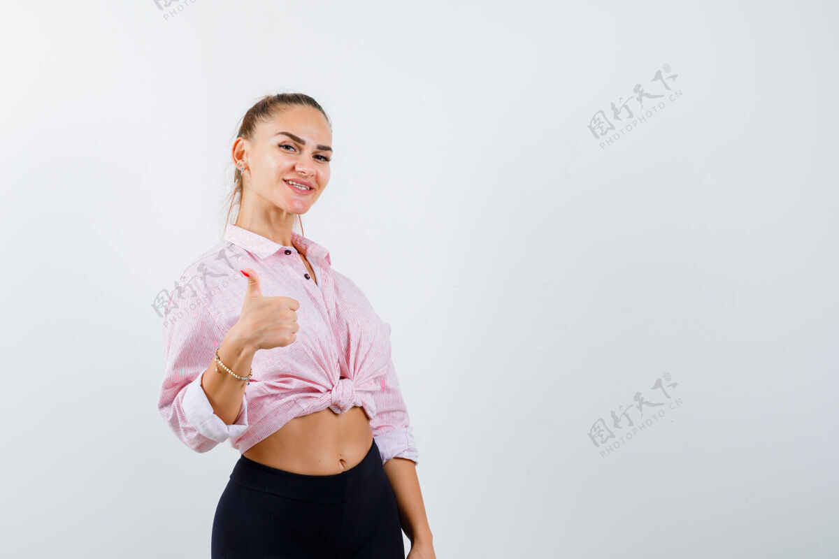 人年轻的女士在衬衫 裤子里竖起大拇指 看起来很快乐 正前方视图假日前面卷发