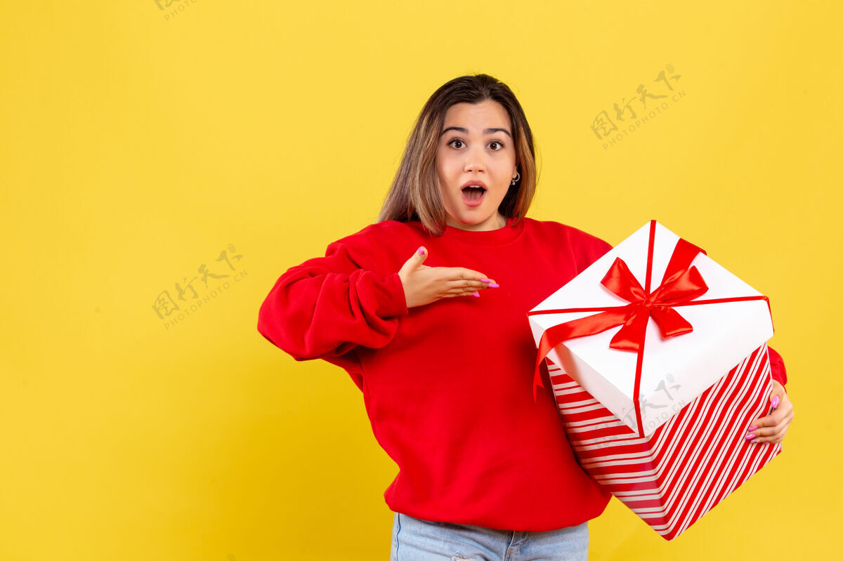 手持黄色背景上手持圣诞礼物的年轻女子的前视图礼物圣诞节年轻女子