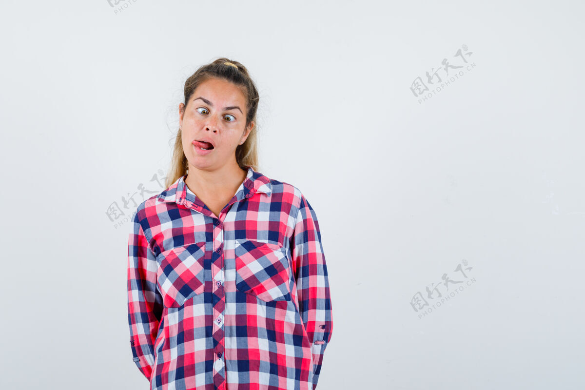 女士年轻女士伸出舌头 眯着眼睛在格子衬衫的肖像 看起来有趣的前视图视图坚持斜视
