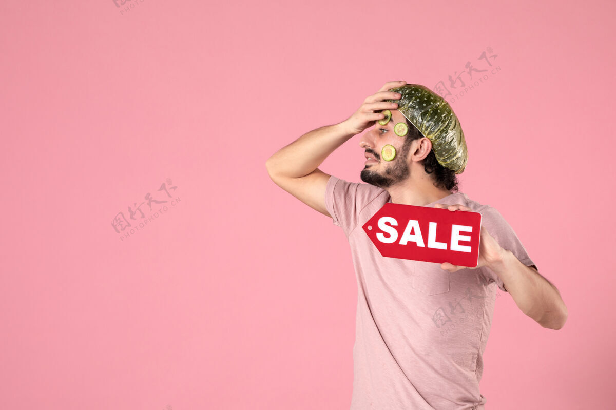 标签正面图：年轻男性 脸上戴着面具 手持粉色背景的销售铭牌视图皮肤销售