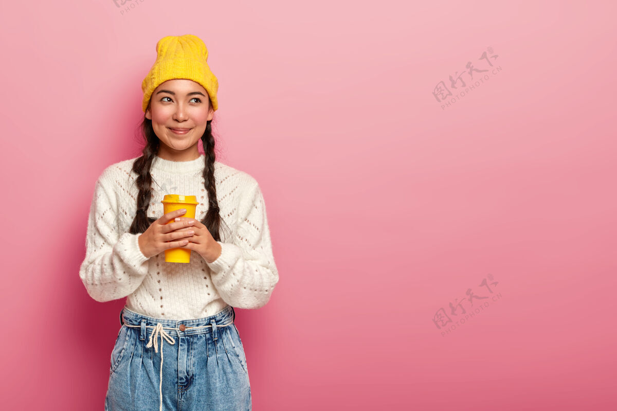 自信梦幻的中国女人喝着外卖咖啡 站在粉色背景下若有所思快乐肖像女人