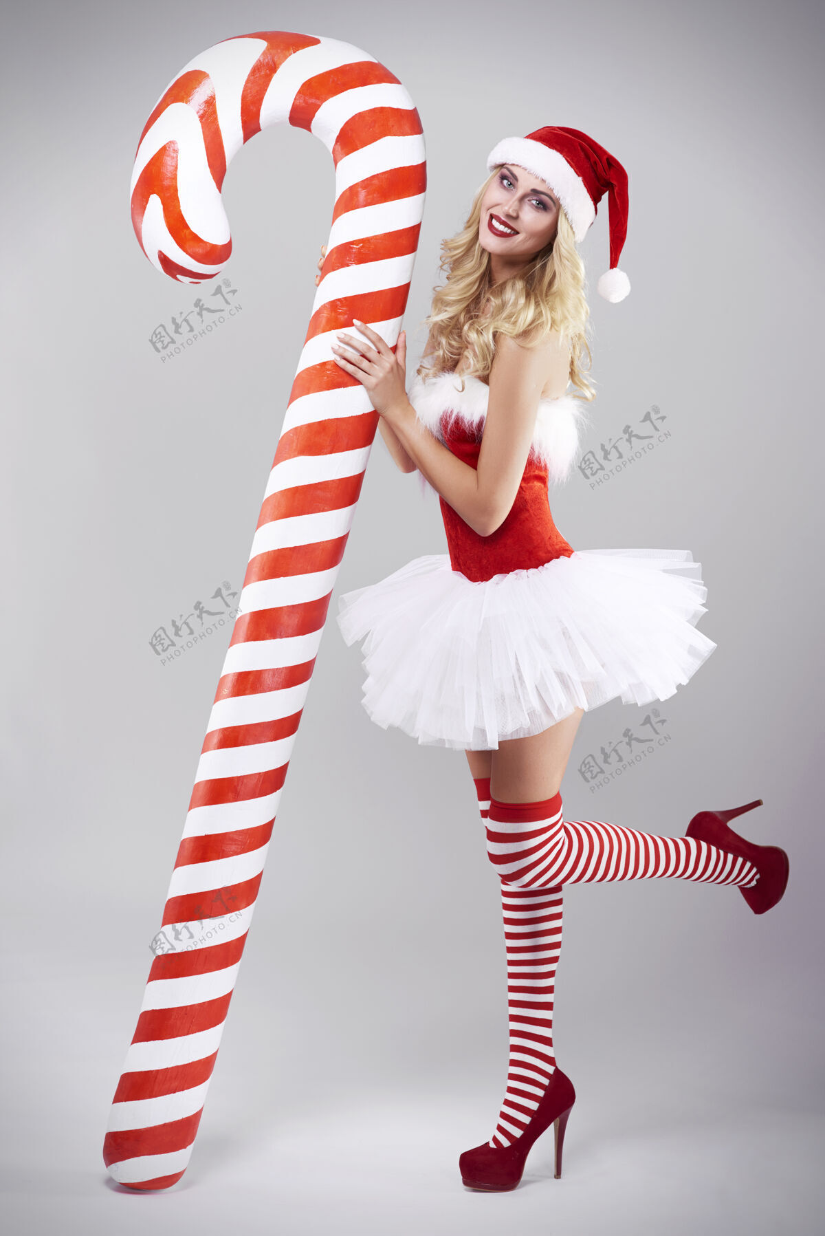 圣诞灰墙上穿圣诞老人服装的性感女人肖像糖果手杖瘦