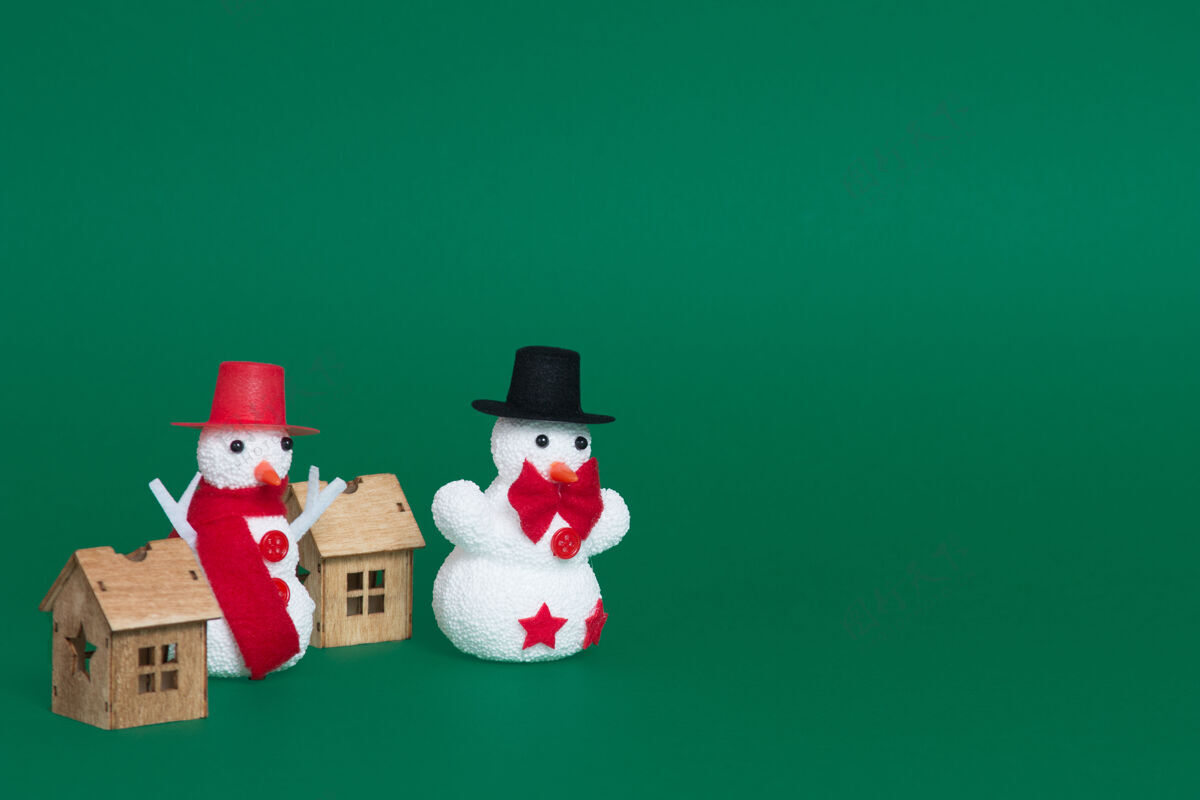 庆祝特写两个雪人和小木屋作为圣诞装饰品的绿色背景帽子装饰品背景
