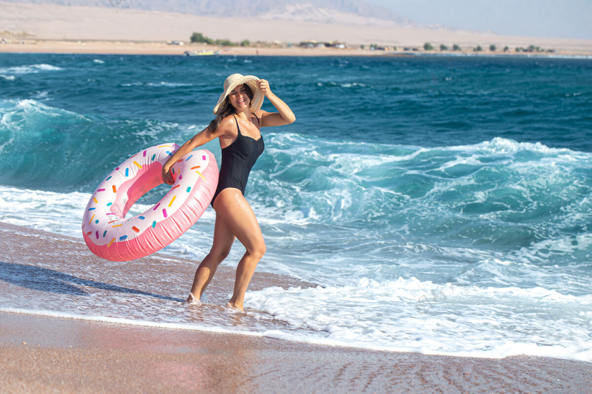 女人一个快乐的年轻女子 在海边有一个甜甜圈形状的游泳圈度假休闲娱乐的概念海滩日落美丽