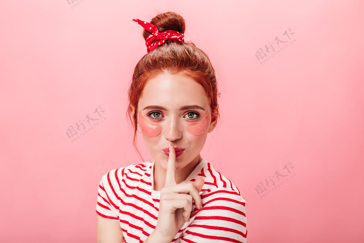 条纹t恤前视图的妇女与眼罩显示秘密标志工作室拍摄的姜女孩触摸嘴唇与手指隔离在粉红色的背景美女女性皮肤