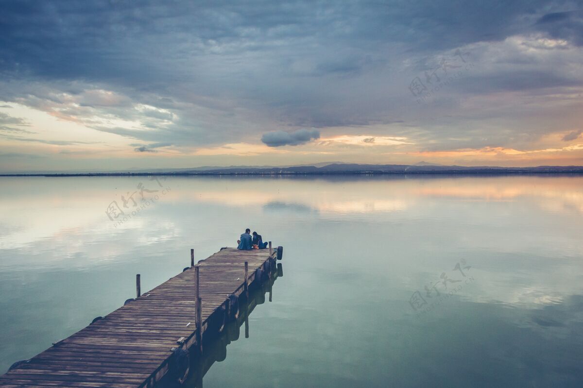 海美丽的情侣坐在美丽的夕阳下的木码头上海滩云浪漫