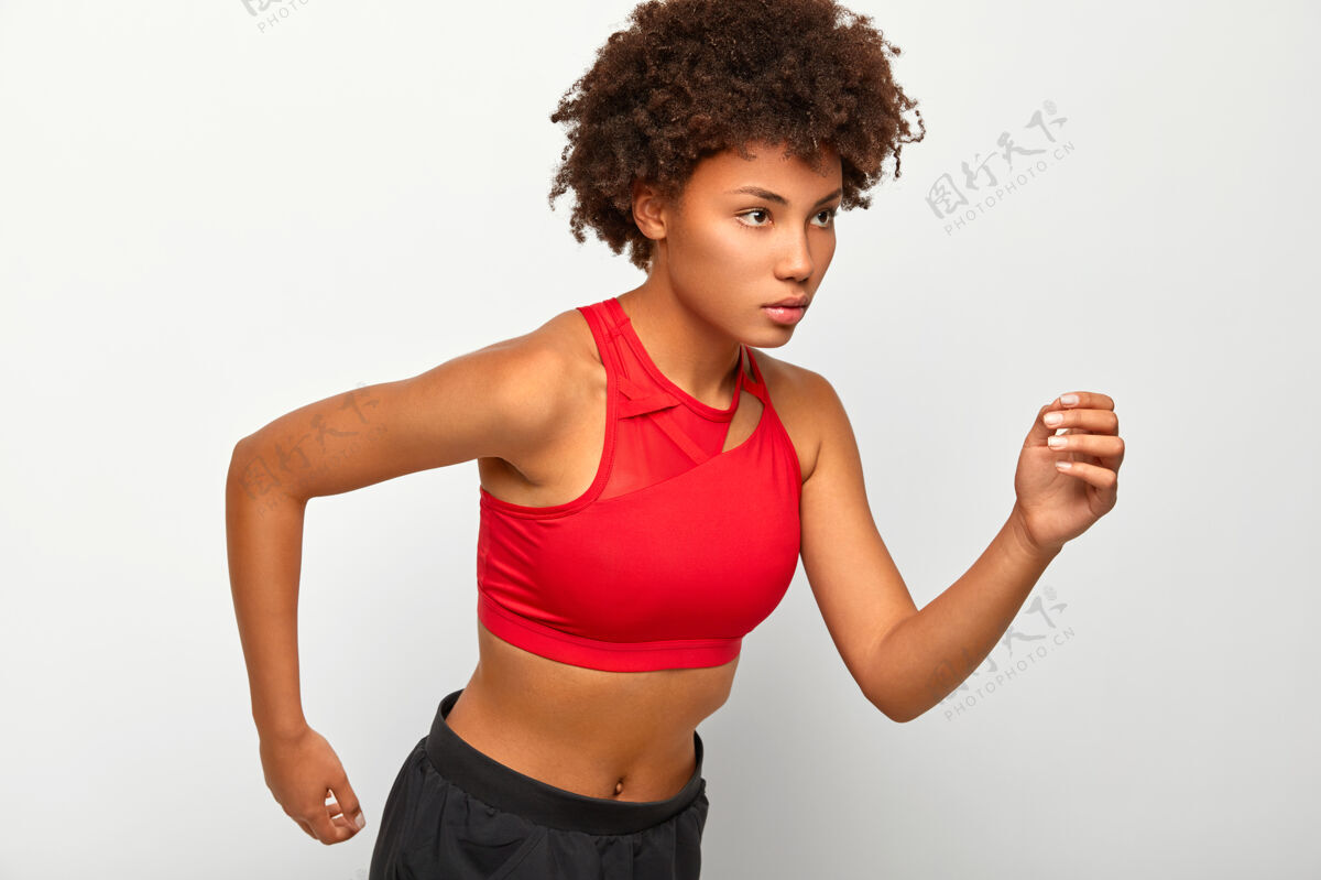 纪律运动自信的女人站在跑步姿势 认真地看着终点 展示耐力 穿红色上衣和短裤 积极地用手臂移动侧身耐力女人