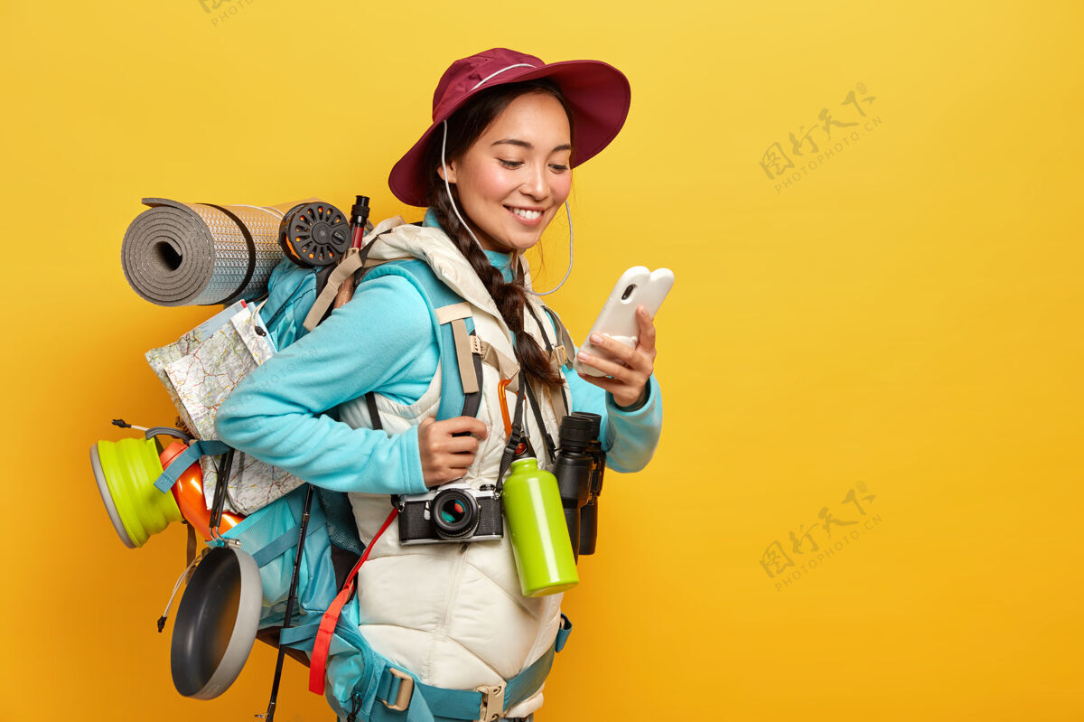 科技积极漂亮的亚洲游客使用现代小玩意导航 戴着帽子和夹克衫 使用双筒望远镜 复古相机 卡雷马特在旅行中站在黄色的墙壁地图休息女人