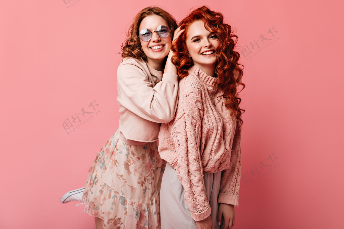 粉色两个最好的朋友微笑着看着相机摄影棚拍摄的快乐迷人的女孩孤立在粉红色的背景漂亮粉色背景卷曲