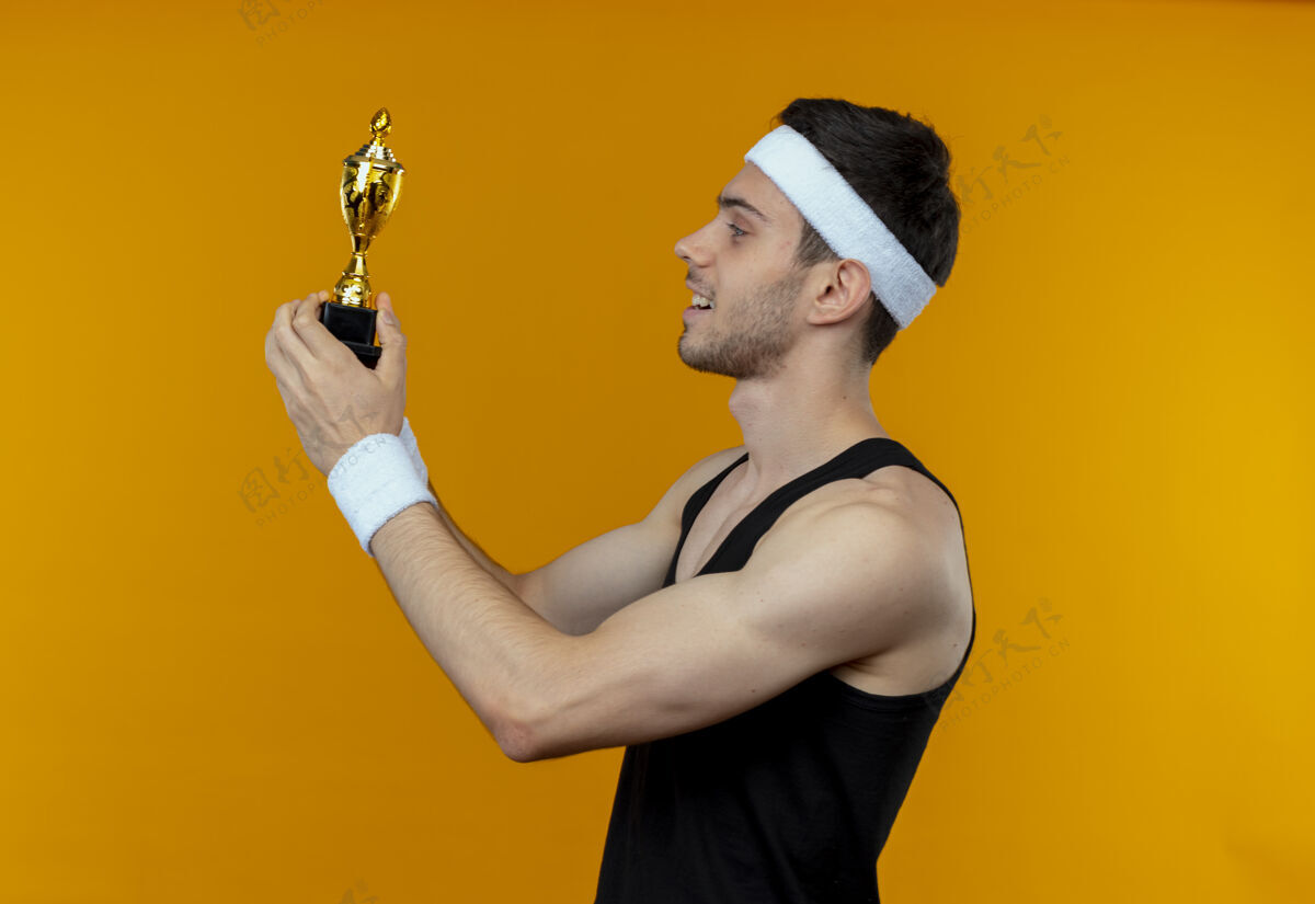 积极戴着头巾的年轻人拿着他的奖杯 站在橘色的墙上 面带微笑地看着我男人年轻运动