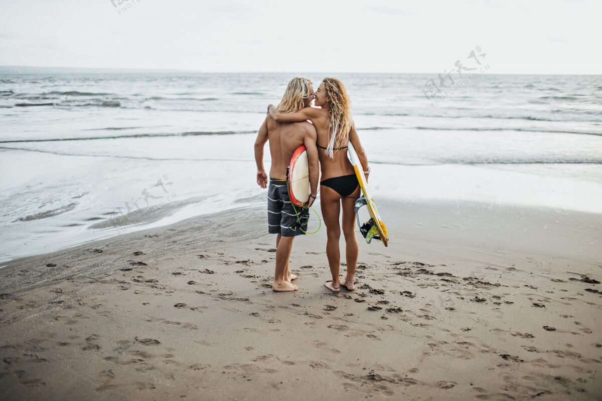 爱照片中的男子和女子在游泳衣举行冲浪板对海微笑女性男性