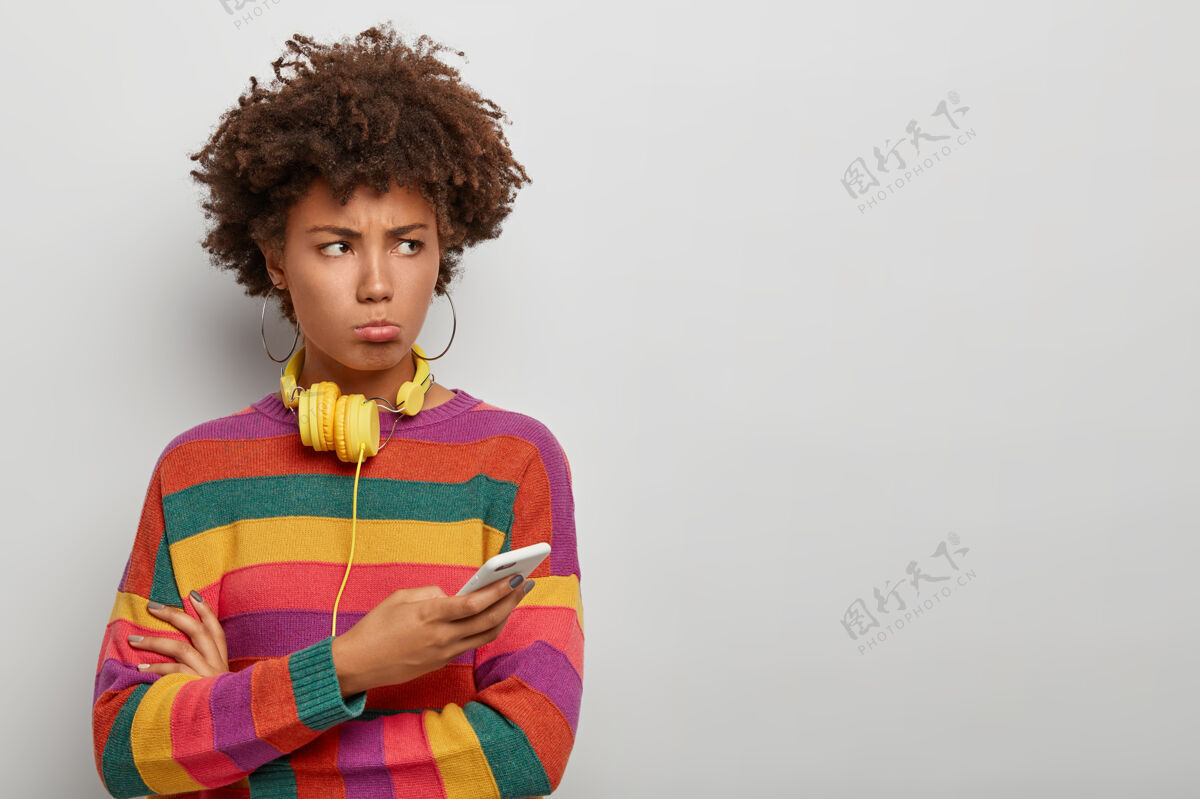 情绪不满的千禧一代非洲女人一边用不满的得罪表情看着 一边用手机条纹女人不高兴