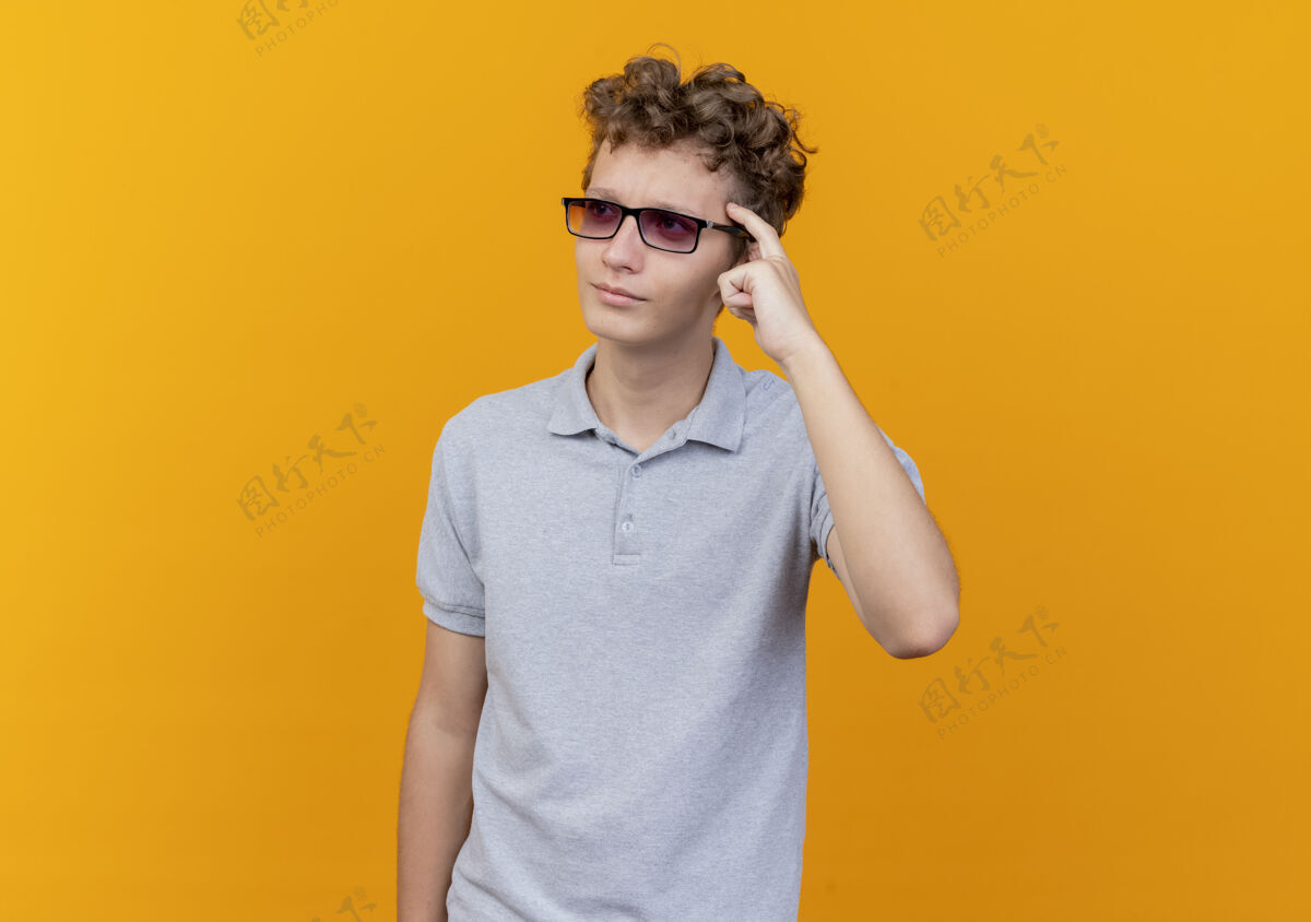 黑色戴着黑眼镜 穿着灰色马球衫的年轻人指着他的太阳穴 试图记住橙色以外的重要事情年轻重要马球