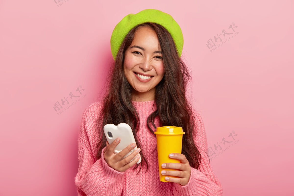 饮料可爱快乐的女人 表情愉快 用手机上网聊天 拿着黄色的咖啡外卖杯通信休闲科技