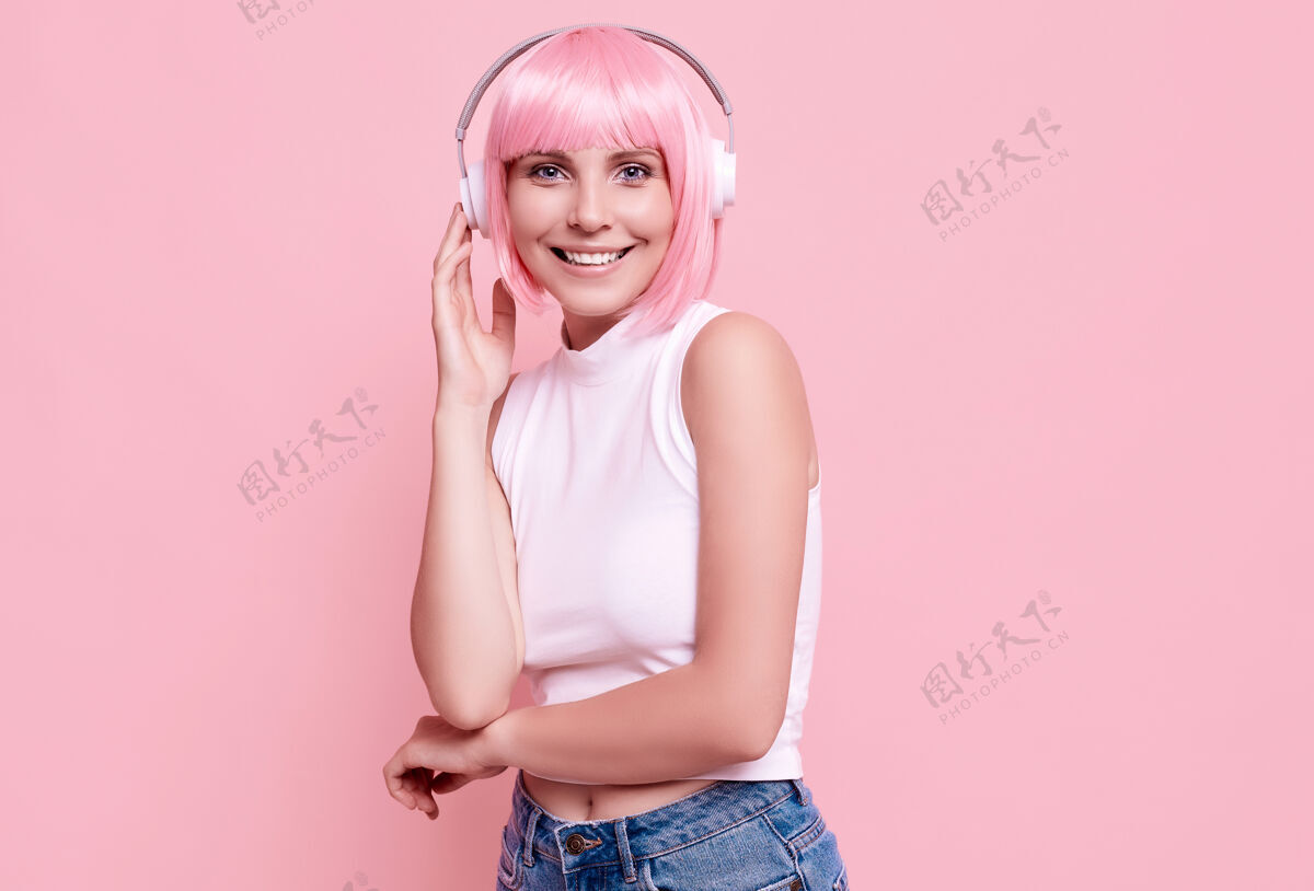 美丽粉红头发的美女肖像在耳机里欣赏音乐无线女性模特