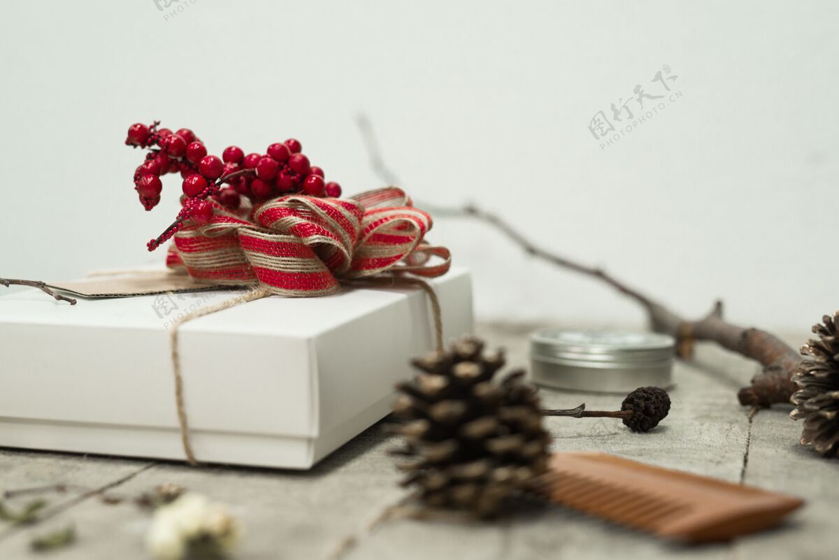 树枝一个白色圣诞礼盒的特写镜头 上面有一个红色的蝴蝶结 放在松果附近的桌子上设计概念灯