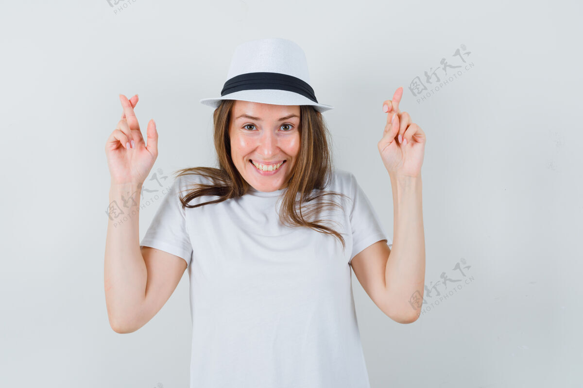 可爱年轻女孩穿着白色t恤 戴着帽子 手指交叉着 看上去很高兴 正面照小手指帽子