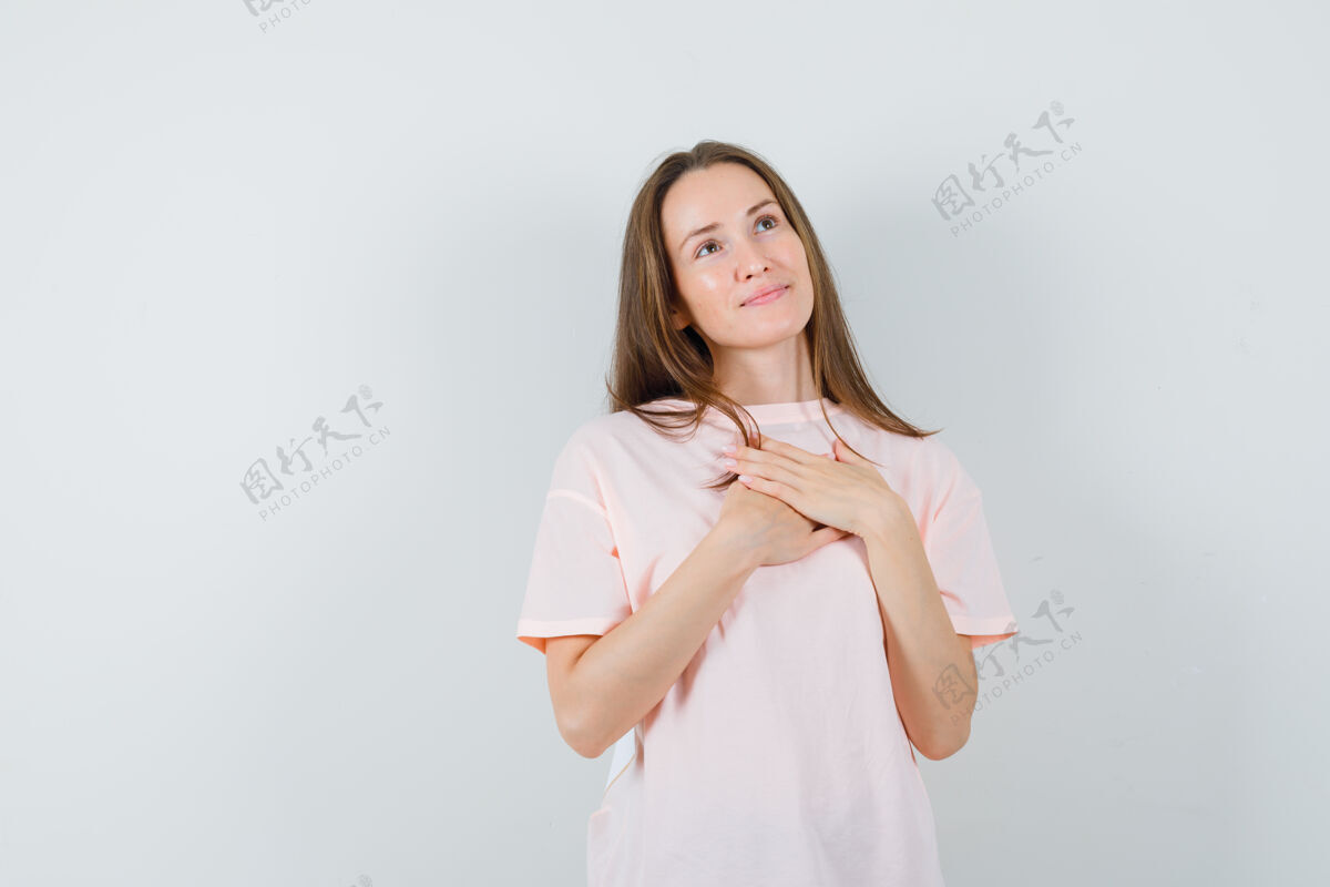 漂亮年轻女性手放在胸前 穿着粉色t恤 看上去充满希望正面图微笑时尚快乐