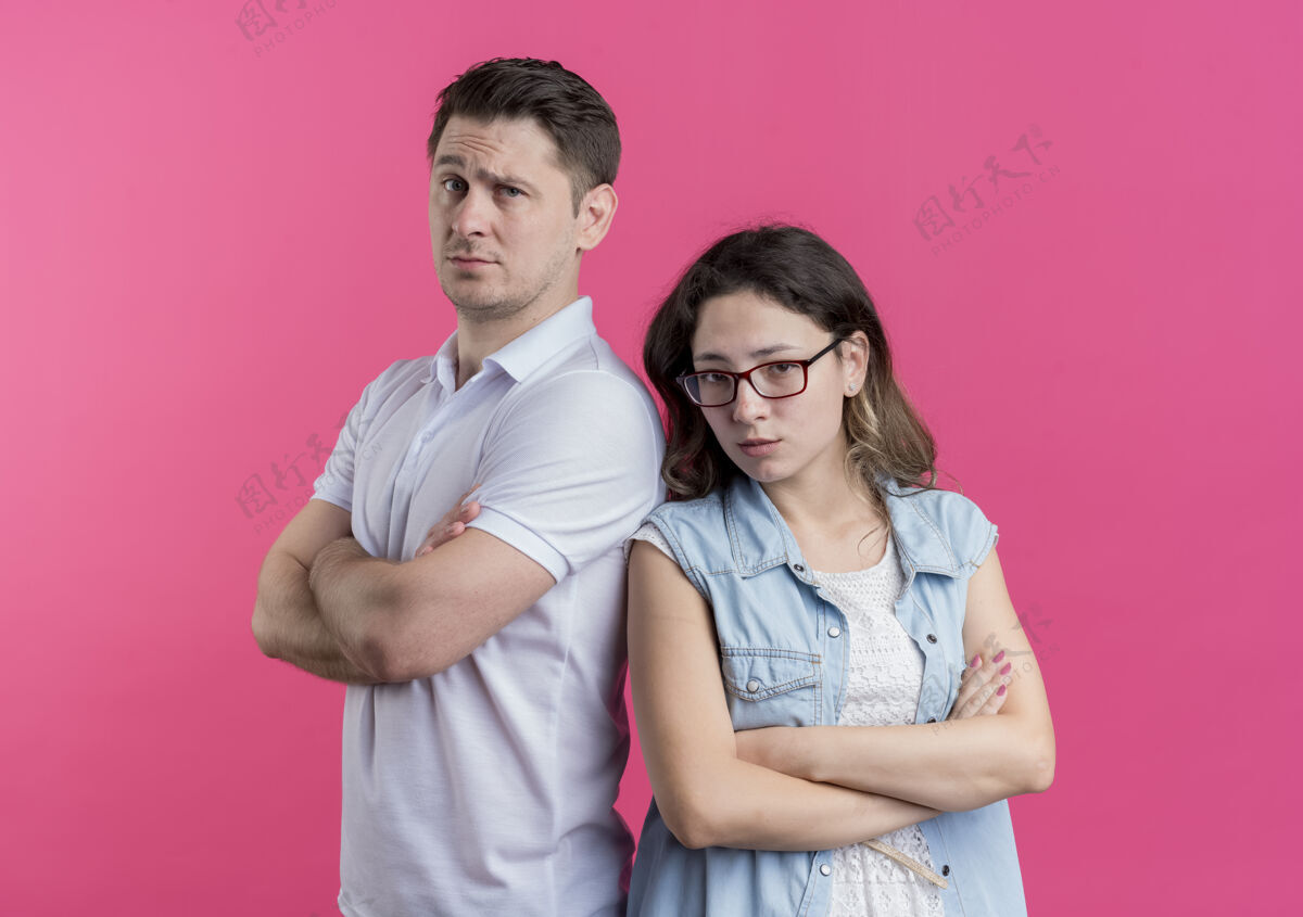 背一对穿着休闲服的年轻夫妇背靠背地站在粉红色的墙上 不高兴地皱着眉头女人男人衣服