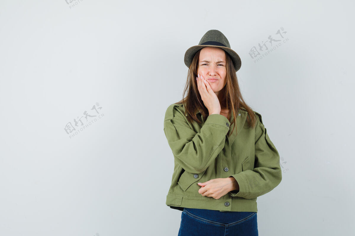 年轻年轻女性穿着夹克 裤子 帽子 牙痛难忍 面容难看裤子微笑帽子