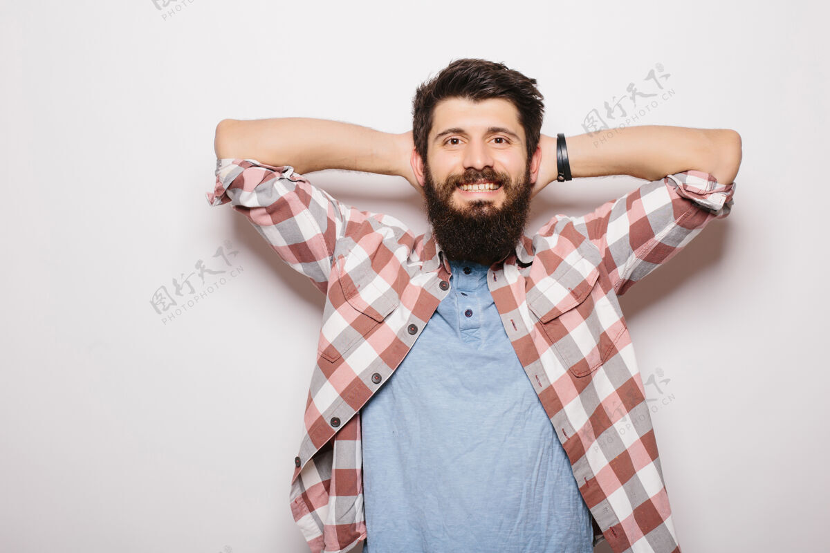 年轻帅气的年轻胡须男人手举着头 站在灰色的墙上看着摄像机自信胡须休闲