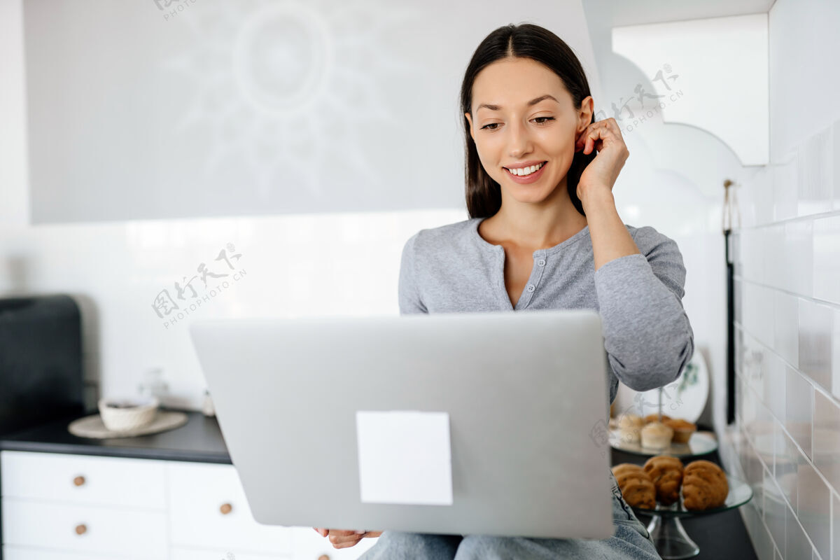 坐着可爱的黑发女人坐在厨房里用笔记本电脑的画面女性笔记本电脑室内