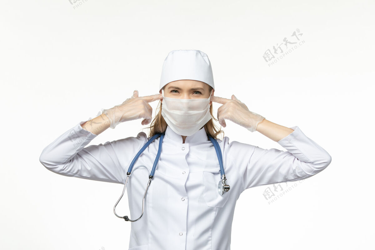 听诊器正面图女医生穿着白色医疗服 戴着无菌口罩 由于冠状病毒 她在白墙疾病上闭上了耳朵 冠状病毒-大流行性疾病正面到期冠状病毒